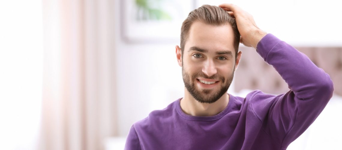 גבר נוגע בשיער עם חולצה סגולה ומחייך